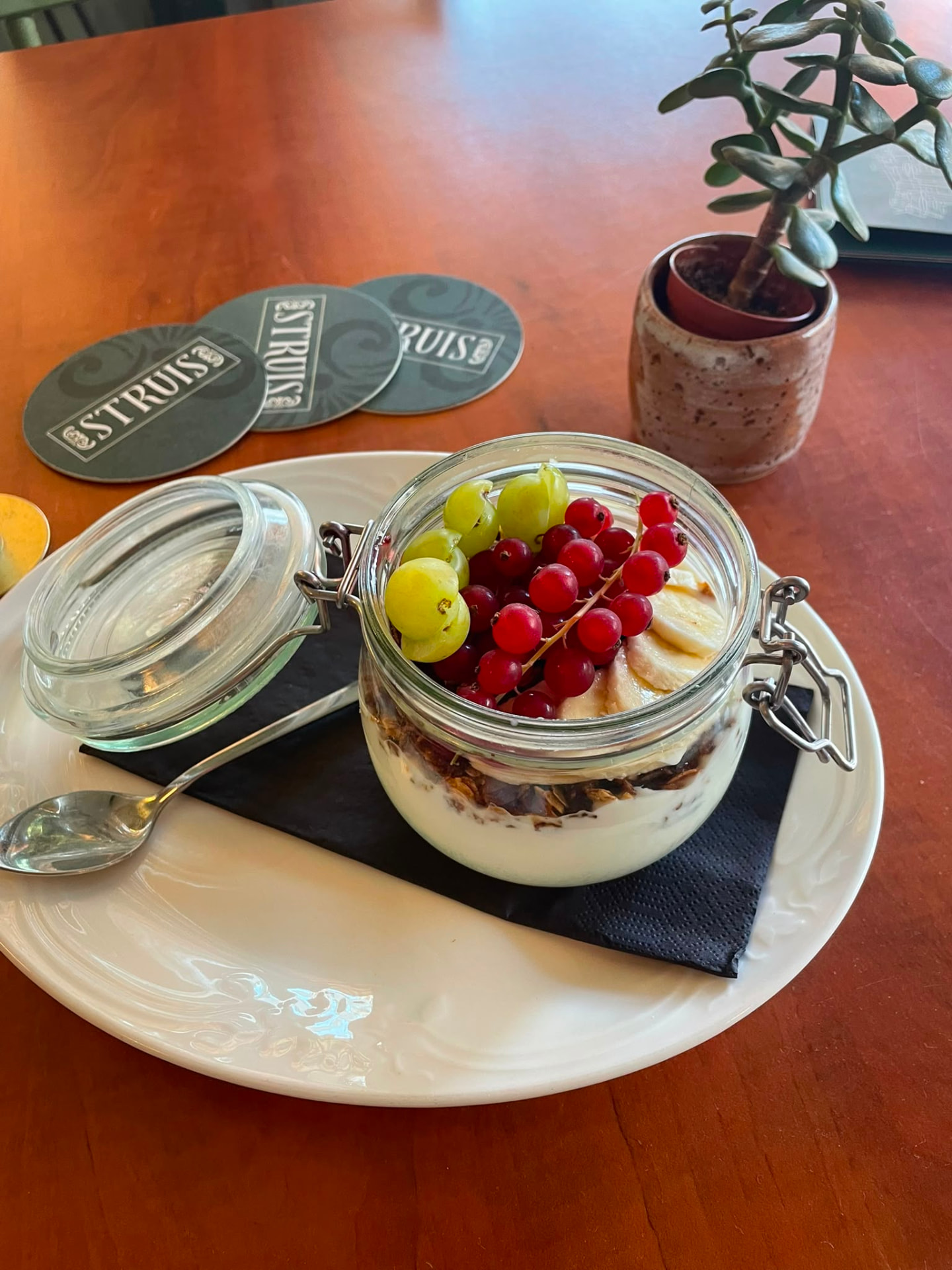 Start your day well in the Schildersbuurt with our fresh organic yoghurt, generously topped with homemade granola and fresh fruit. Fresh breakfast yoghurt with crunchy granola, banana, redcurrants and grapes served in a glass jar at café Struis in Groningen.